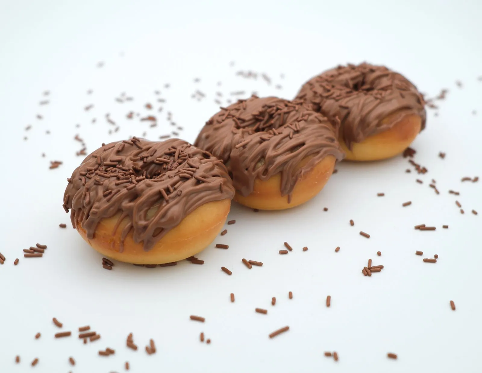 Three chocolate-glazed donuts with sprinkles on a white background, perfect for food enthusiasts.
